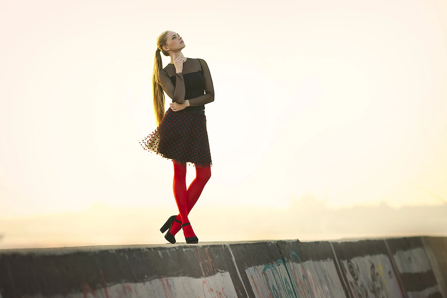 Woman in Black Dress and Red Tights on Concrete Wall