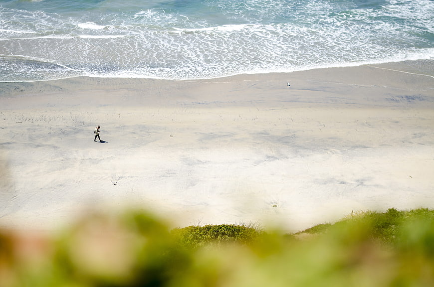 Aerial view of lone person walking on sandy beach with ocean waves