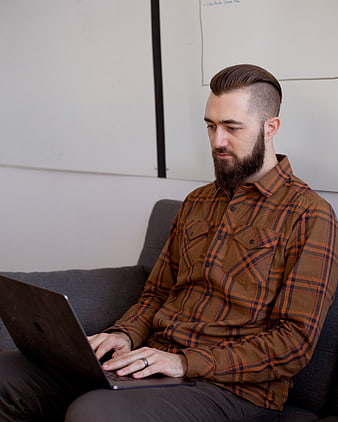 Bearded man typing on laptop on couch