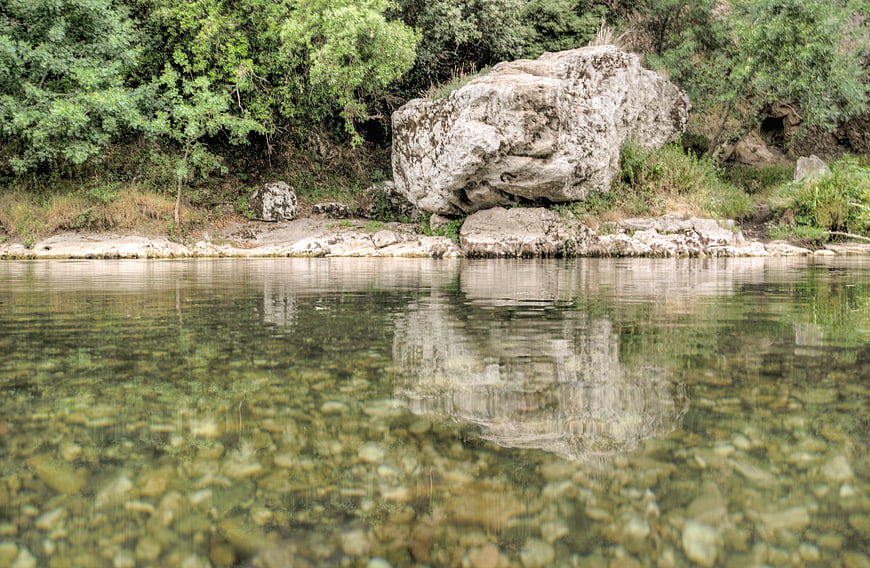 Clear river water reflecting large boulder and green forest