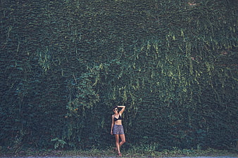 Woman in black bikini top standing against ivy wall