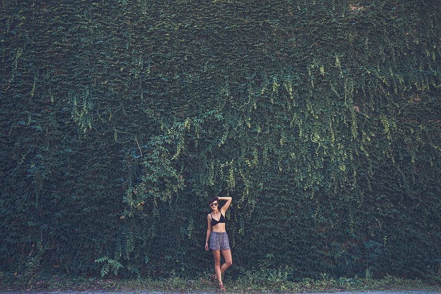 Woman in black bikini top standing against ivy wall