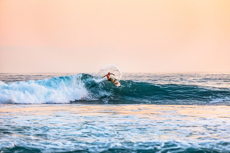 Surfer riding a wave at sunset with pastel sky