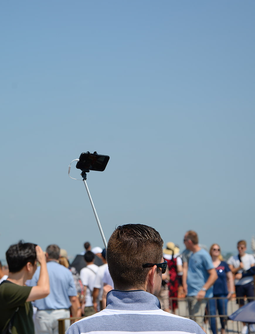 Man holding selfie stick in crowd against blue sky