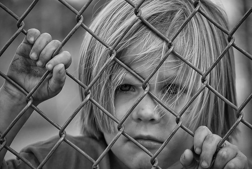 Sad young boy looking through chain link fence