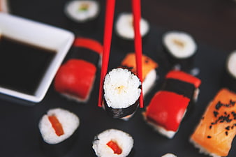 Red Chopsticks Holding Sushi Over Dark Platter