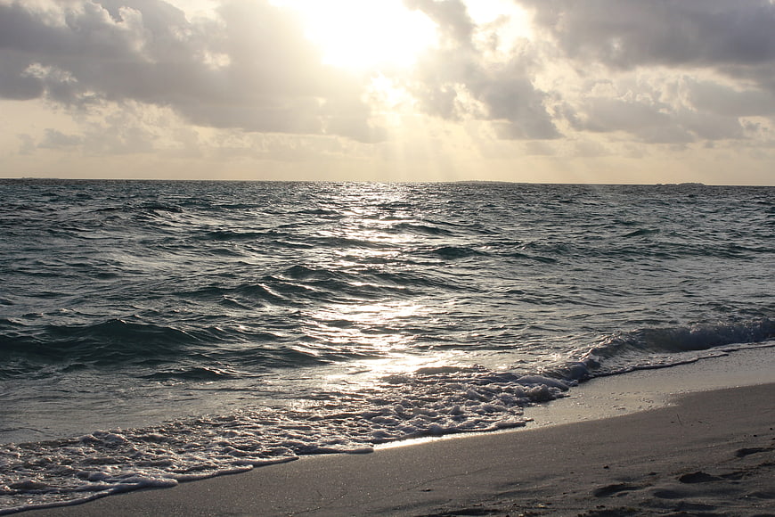 Sunlight breaking through clouds over ocean waves at dusk