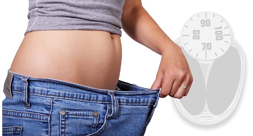 Woman in oversized jeans holding weight scale
