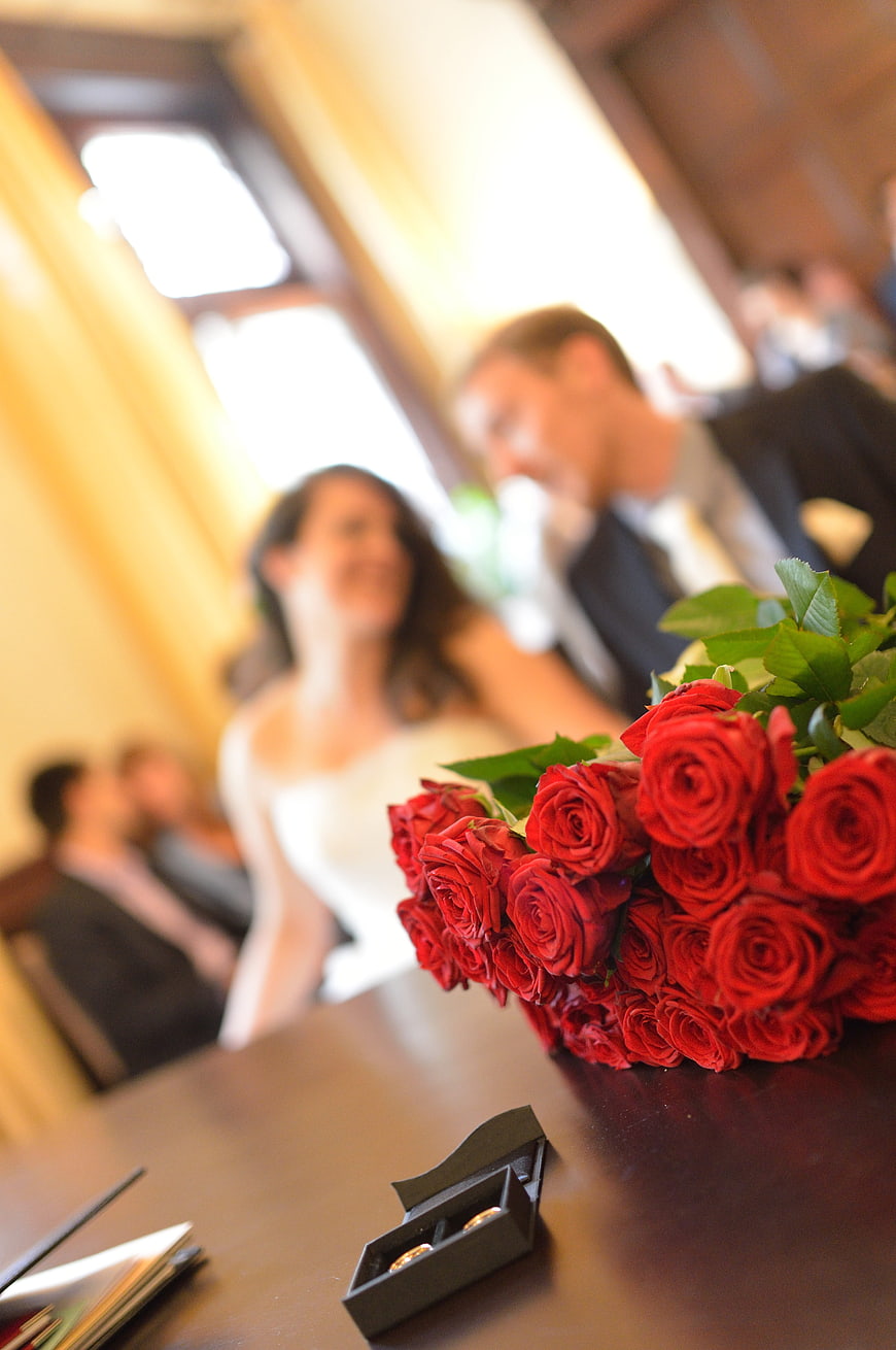 Red Roses and Wedding Rings on Table with Blurred Couple