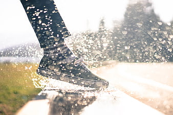 Close-up of a sneaker splashing in a puddle with rain droplets