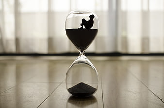 Silhouette of person sitting in hourglass on wooden floor
