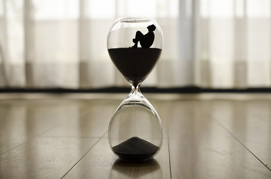 Silhouette of person sitting in hourglass on wooden floor
