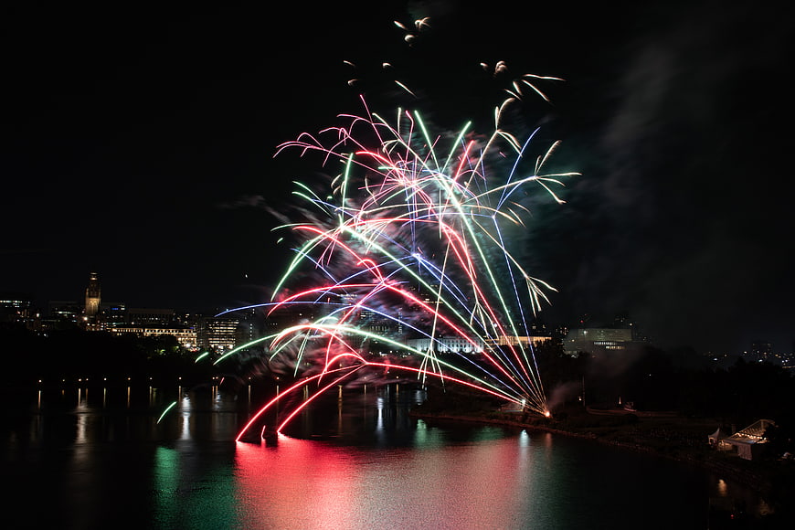 Colorful fireworks exploding over a river at night with city skyline