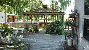 Rustic wooden gazebo on a backyard deck with garden plants and trees
