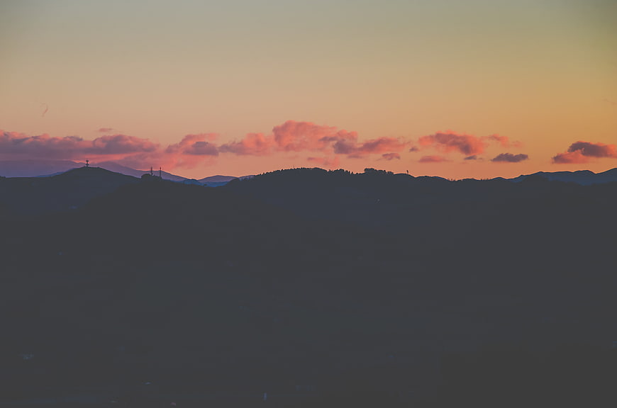 Silhouette of rolling hills against a pink and orange sunset sky