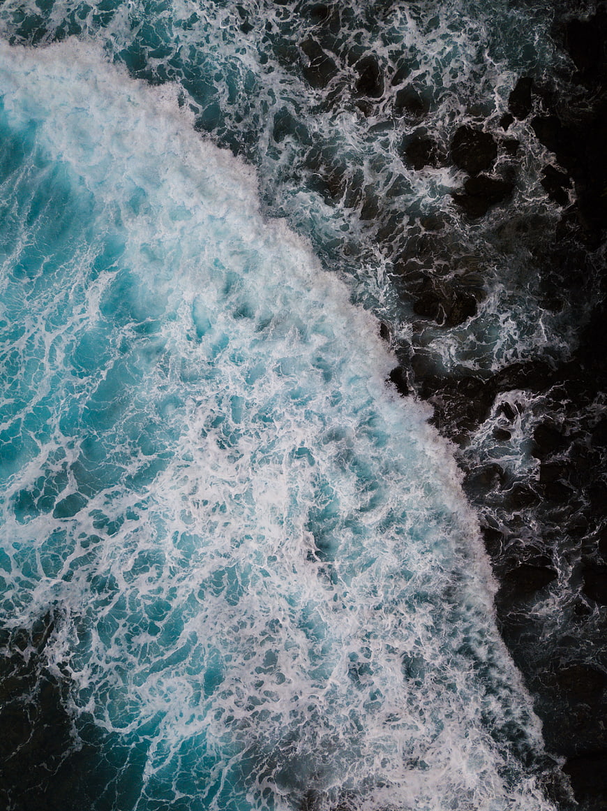 Aerial View of Turquoise Waves Crashing on Dark Rocks
