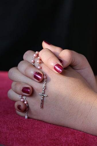 Close-up of hands holding a rosary with red manicure