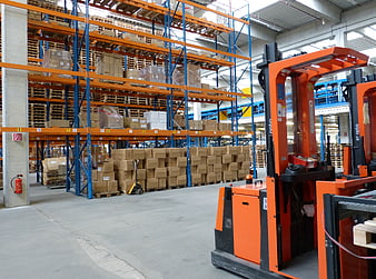 Orange Forklift in Industrial Warehouse with Blue Racking and Cardboard Boxes