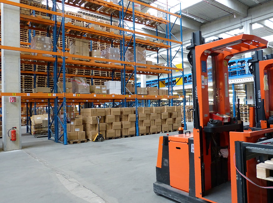 Orange Forklift in Industrial Warehouse with Blue Racking and Cardboard Boxes