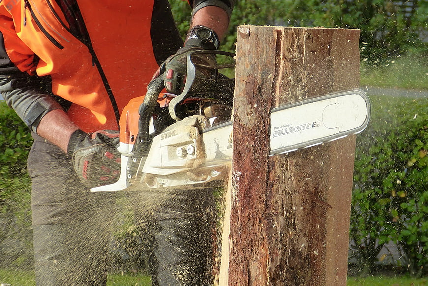 Worker Cutting Wood with Chainsaw Outdoors