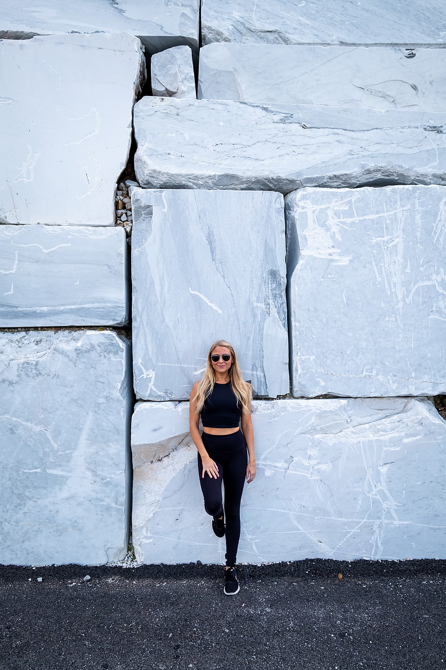 Blonde woman in black activewear posing against large marble blocks