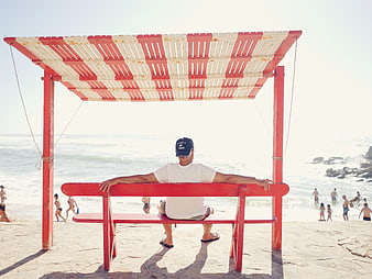 Senior man relaxing on red lifeguard chair at sunny beach