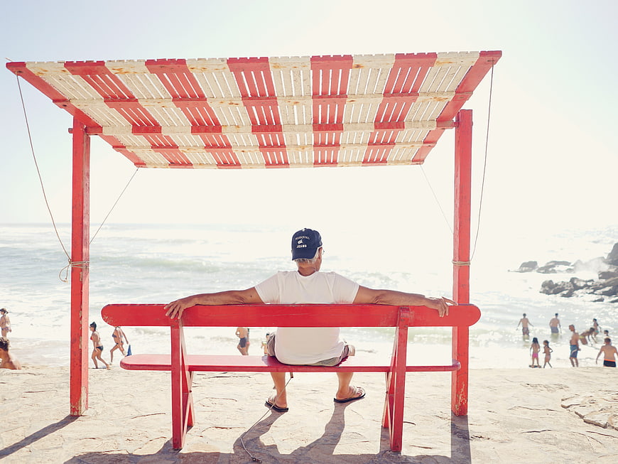 Senior man relaxing on red lifeguard chair at sunny beach