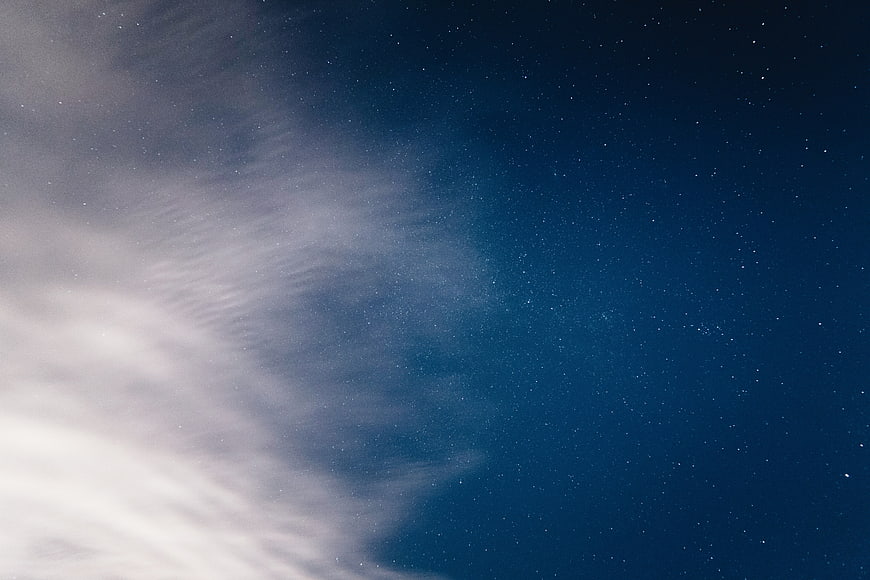 Starry night sky with wispy clouds and deep blue gradient