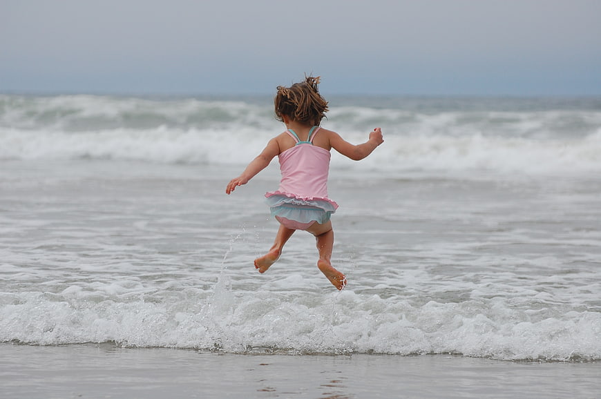Little Girl Jumping in Ocean Waves at Beach