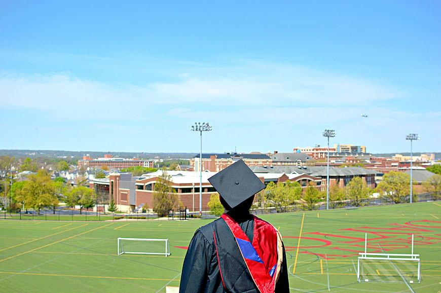 Graduate in Cap and Gown Overlooking College Campus