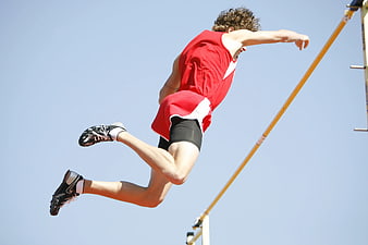 Pole vaulter in red uniform jumping against blue sky