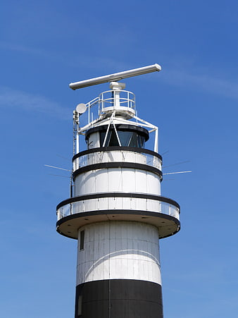 Modern white and black lighthouse tower with radar equipment against blue sky