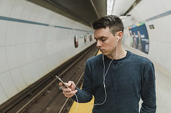 Young man using smartphone with earphones in subway station
