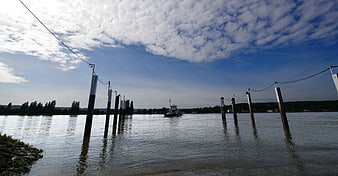 Wide River Scene with Navigation Posts and Boat Under Cloudy Sky