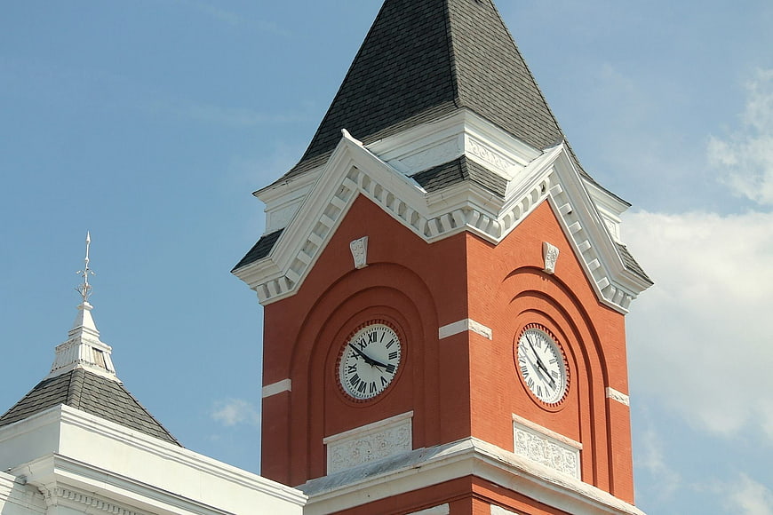 Red brick clock tower with white trim against blue sky
