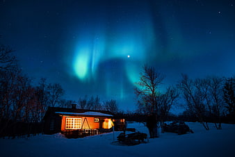 Aurora Borealis over a cozy cabin in snowy winter night