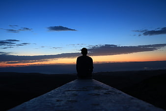 Silhouette of Man Sitting on Wall Watching Sunset