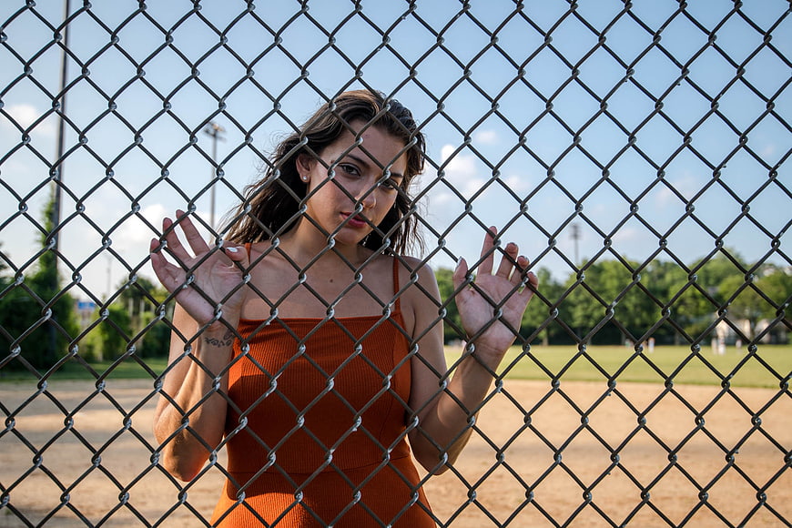 Young woman in orange dress behind chain-link fence