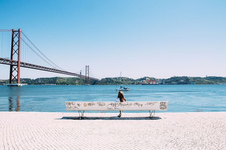 Woman sitting on bench overlooking 25 de Abril Bridge in Lisbon