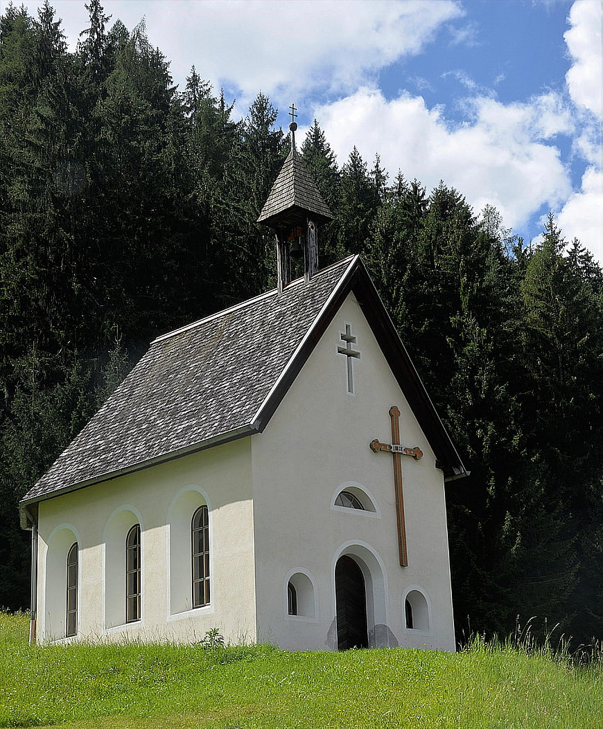 Small white chapel in green meadow with forest background