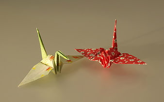 Two colorful origami cranes in flight against a neutral beige background