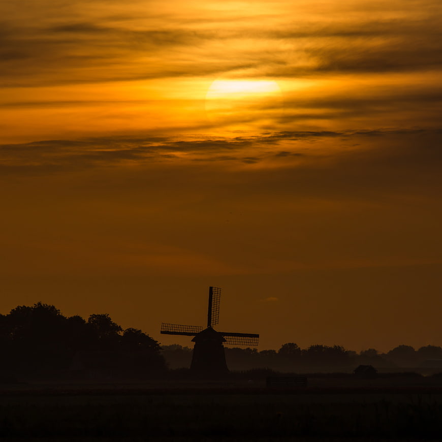 Silhouette of Dutch Windmill Against Golden Sunrise Sky