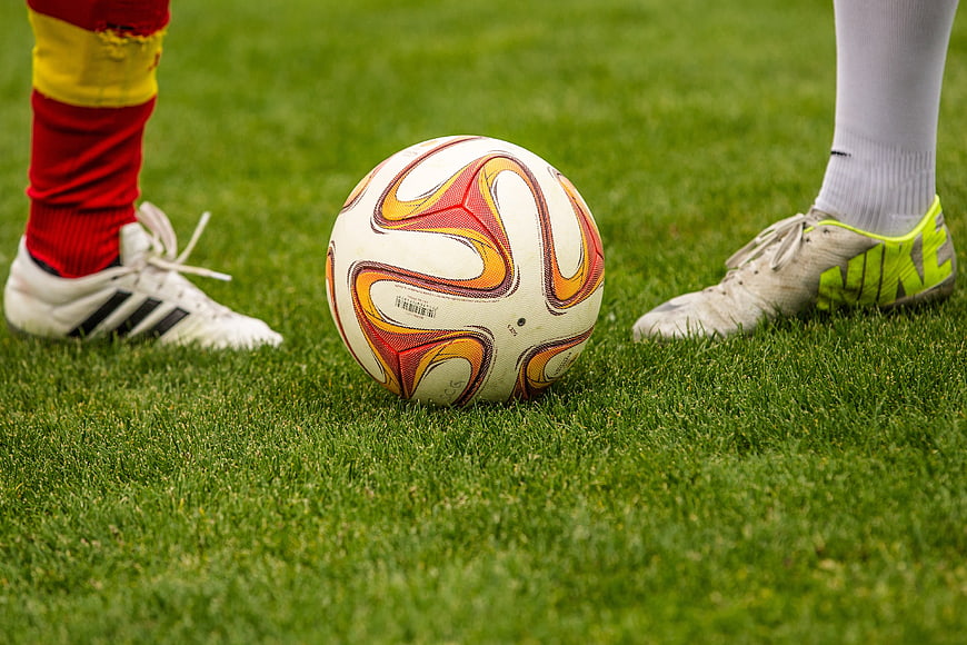 Soccer ball between two players' feet on grass field