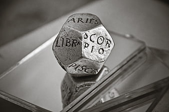 Black and white close-up of a d20 die with zodiac signs