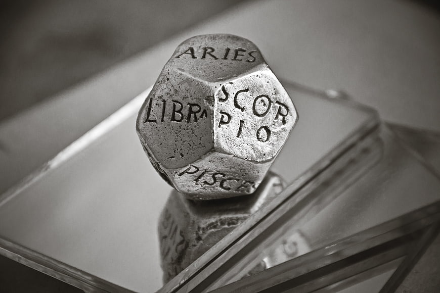 Black and white close-up of a d20 die with zodiac signs