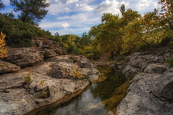 Serene rocky riverbed with autumn foliage and blue sky