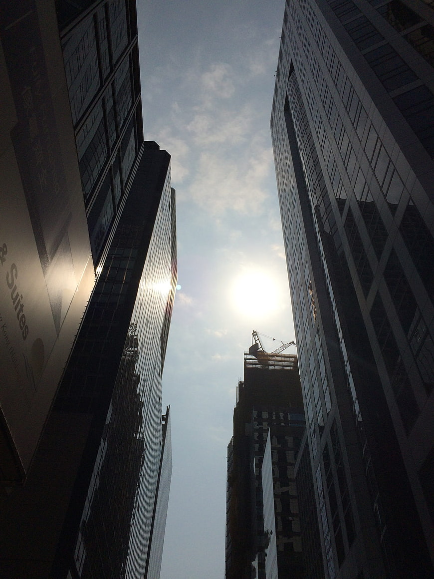 Low angle view of modern skyscrapers and construction crane against bright sky