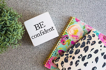 Flat lay of notebooks and be confident sign