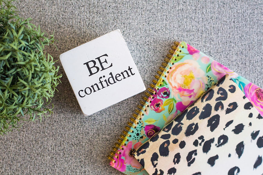 Flat lay of notebooks and be confident sign