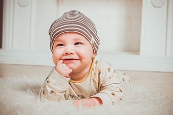 Cute smiling baby boy in striped hat on white rug